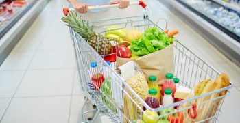 Consumer cart with various food products being pushed by woman